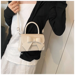 Detail of a creamy white bow handbag showing texture, handle, and adjustable shoulder strap