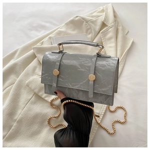Close-up of grey crinkled patent leather handbag with golden sphere chain and buckle