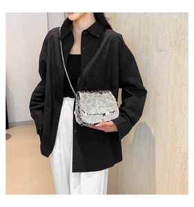 Detail shot of a silver sequin crossbody bag with a metal chain strap on a model