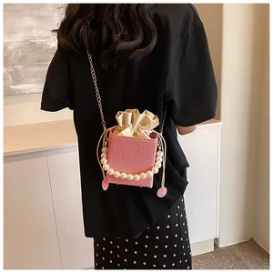 Détail du sac seau tissé rose avec poignée en perles et bandoulière en chaîne