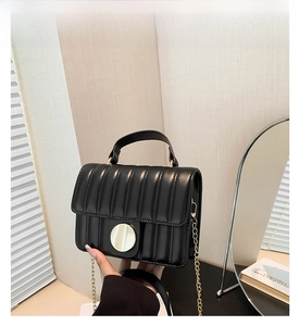 Detail of black quilted leather handbag featuring a gold circular lock and chain strap