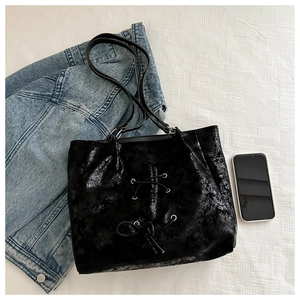 Detail of black tote bag with bow accent and glossy cracked texture on white fabric
