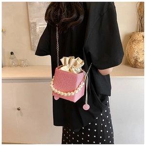 Detail of pink woven bucket bag featuring pearl handle and gold chain strap in home setting
