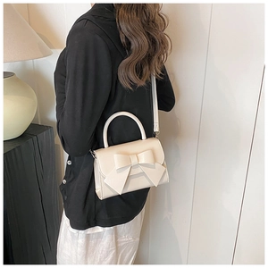 Detail view of cream bow handbag worn crossbody by a model in a modern interior