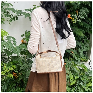 Detail of hand-woven straw crossbody bag with brown leather trim and gold metal lock
