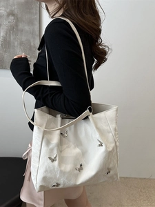 White bucket bag with silver butterfly charms and slim shoulder straps on a model