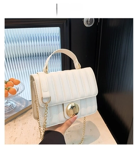 Close-up of white quilted leather texture with gold circular clasp and metal chain