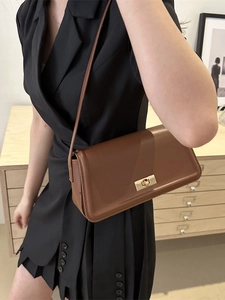 Minimalist brown leather tote bag with gold buckle closure worn as a shoulder bag