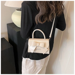 Side view of cream bow handbag worn as crossbody bag by model in a minimalist setting