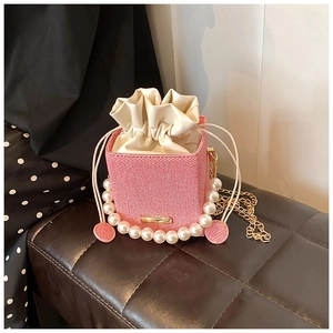 Detailed view of pink woven bucket bag with pearl handle and golden chain strap