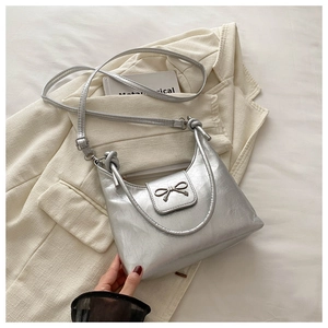 Détail du sac croissant argenté avec nœud métallique et texture froissée sur un blazer