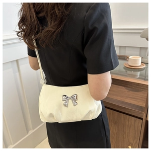 Close-up of cream pleated shoulder bag with a metallic silver bow accent and slim strap
