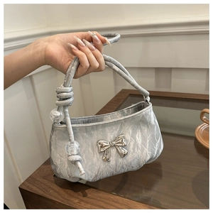 Detail of silver pleated handbag with metallic bow and decorative bead on the strap