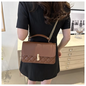 Braune Stepptasche mit goldener Kette und Verschluss getragen von einem Modell
