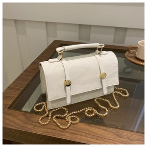 Detail of white textured leather handbag with gold rivets and snake chain strap