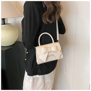 Detail of a beige bow handbag shown on a model's back for stylish crossbody wear