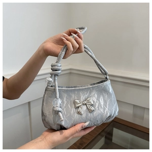 Detail of silver handbag with metallic bow ornament and beaded handle on white background