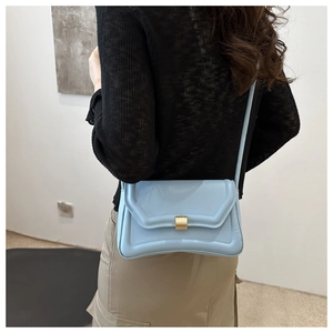 Detail of light blue crossbody saddle bag with gold metal lock and quilted leather texture
