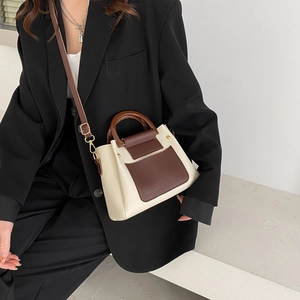 Detail of contrast stitch patchwork bag with wooden handle and adjustable brown shoulder strap