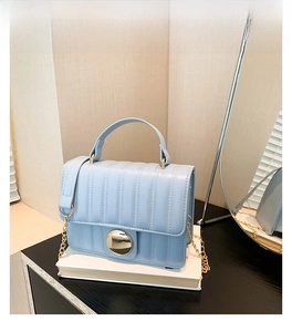 Detail of light blue quilted crossbody bag with gold metallic snap and chain strap