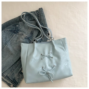 Detail of light blue tote bag with decorative ribbons and bow design on white background