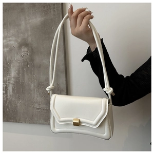Detail of white saddle bag with golden rectangular clasp and decorative knot strap