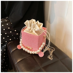 Detailed shot of pink woven bucket bag with pearl handle and golden chain strap