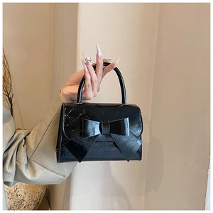 Close-up of a black textured leather handbag with a large decorative bow and top handle