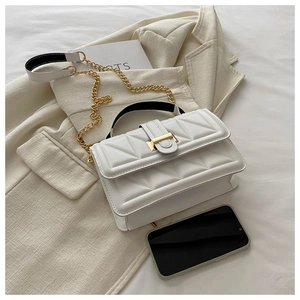 Close-up of white quilted handbag with gold chain strap on professional chic blazer