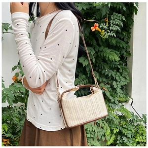 Outdoor shot of a woven straw crossbody bag with brown leather trim and gold hardware