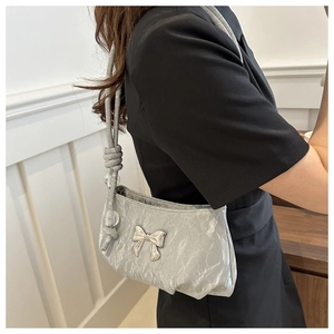Detail of silver pleated underarm bag with metallic texture and bow ornament