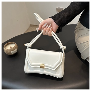 Detail of white saddle bag showing gold metal buckle and knotted shoulder strap design