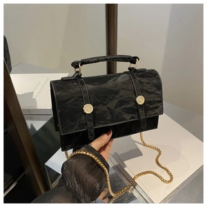 Detail shot of the black crinkled texture faux leather and golden buckle of the handbag