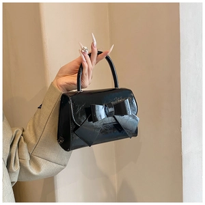 Detail of a black patent leather handbag featuring a large bow and glossy finish