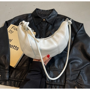 Close-up of white croissant bag with vertical stitching and knot detail on black leather