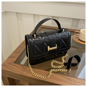 Detail of black quilted leather crossbody bag with gold hardware on a coffee table