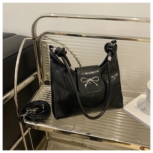 Détail d'un sac en cuir noir brillant avec un nœud métallique argenté et une bandoulière