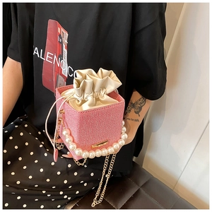 Détail d'un sac seau rose tressé avec poignée en perles et bandoulière chaîne dorée