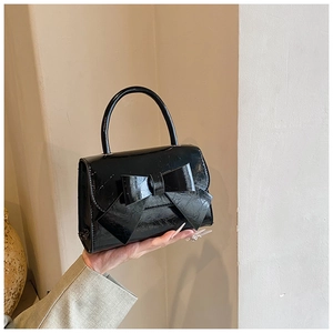 Detail of glossy black patent leather handbag featuring a large decorative bow and top handle