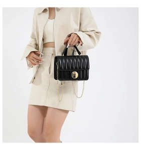Detail of black quilted shoulder bag featuring a round gold buckle and metal chain strap