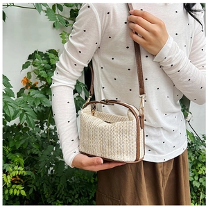 Detail of hand-woven straw crossbody bag featuring brown leather trim and golden hardware