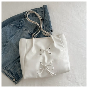 Detail of white tote bag with bow knots, silver eyelets, and shimmery leather texture