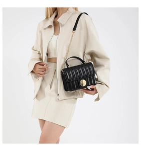 Detail of black quilted crossbody bag featuring a gold round clasp and chain strap