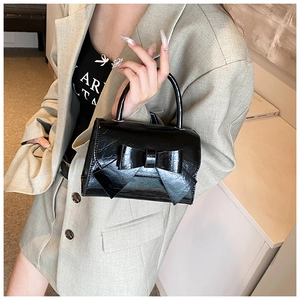Detail of glossy black patent leather handbag with large bow and circular handle