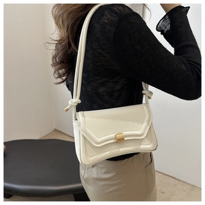 Close-up of white minimalist shoulder bag with matte gold buckle and knotted rope strap