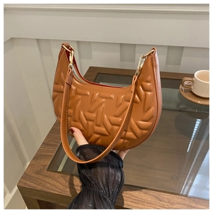 Detail of caramel brown quilted crescent underarm bag with red lining and gold hardware