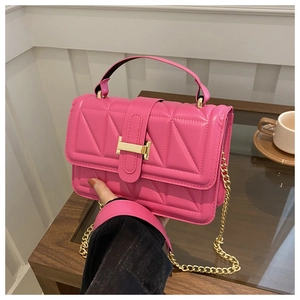 Detail of fuchsia crossbody bag with triangle quilting and gold chain strap held by hand