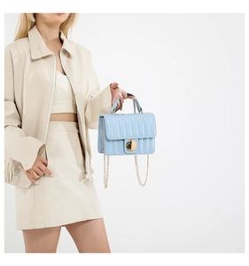 Close-up of light blue pleated handbag featuring a gold round lock and metal chain strap