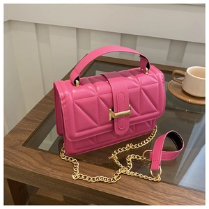Detail of rose red quilted crossbody bag with golden metal buckle on glass table