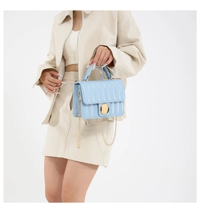 Detail of light blue quilted handbag with gold chain strap and metal turn-lock closure